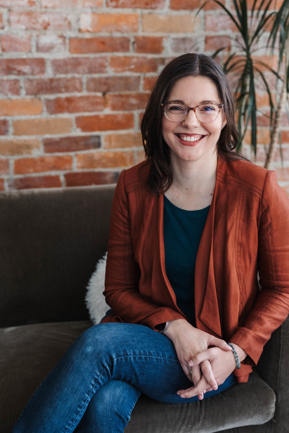 A photograph of the author, sitting on an emerald velvet couch in a trendy Pioneer Square exposed-brick loft. She is smiling, her legs crossed and hands clasped in her lap. She is wearing her favorite jacket. 